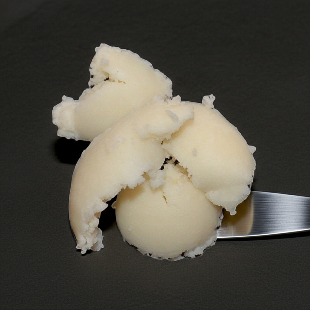 Raffinierte Mangobutter – cremige, helle Pflanzenbutter auf Spatel, Nahaufnahme der Textur, geeignet für DIY-Kosmetik.